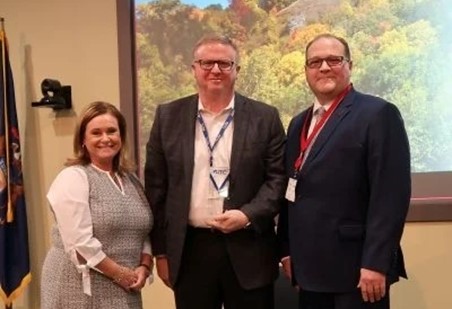 Three people posed for a photo in front of landscape portrait in office