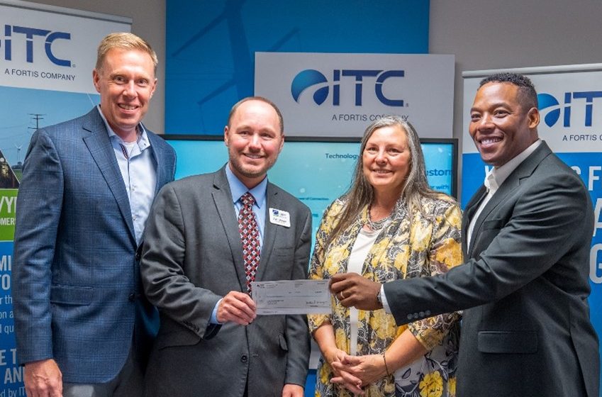 Four people posed for picture in front of ITC banners holding donated check