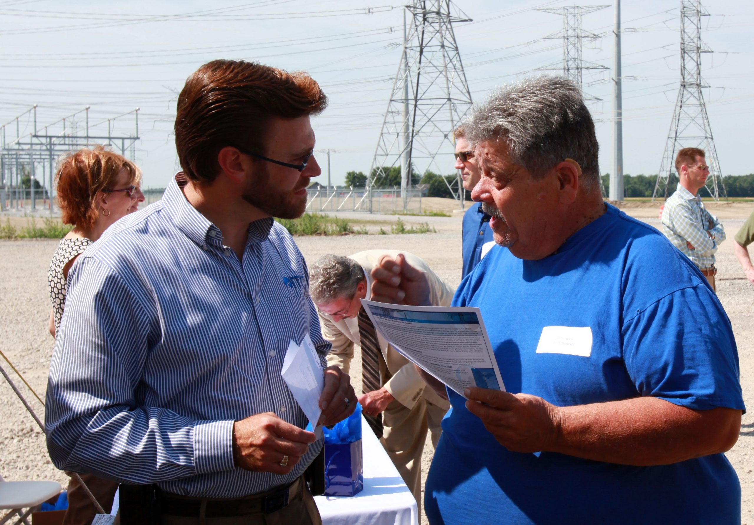 Two people in discussion with paper in their hands and in front of electrical transmission lines.