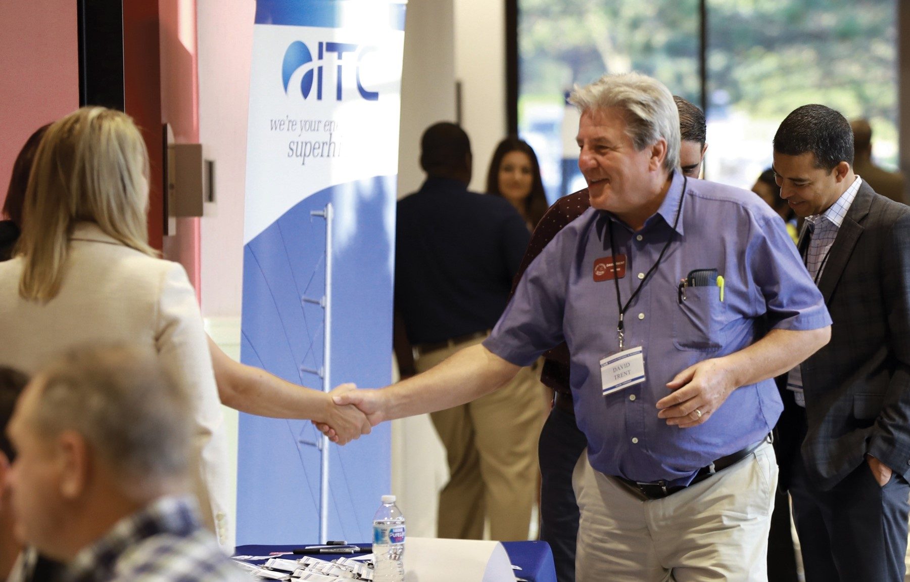 Two people shaking hands over ITC promotional booth surrounded by a crowd.