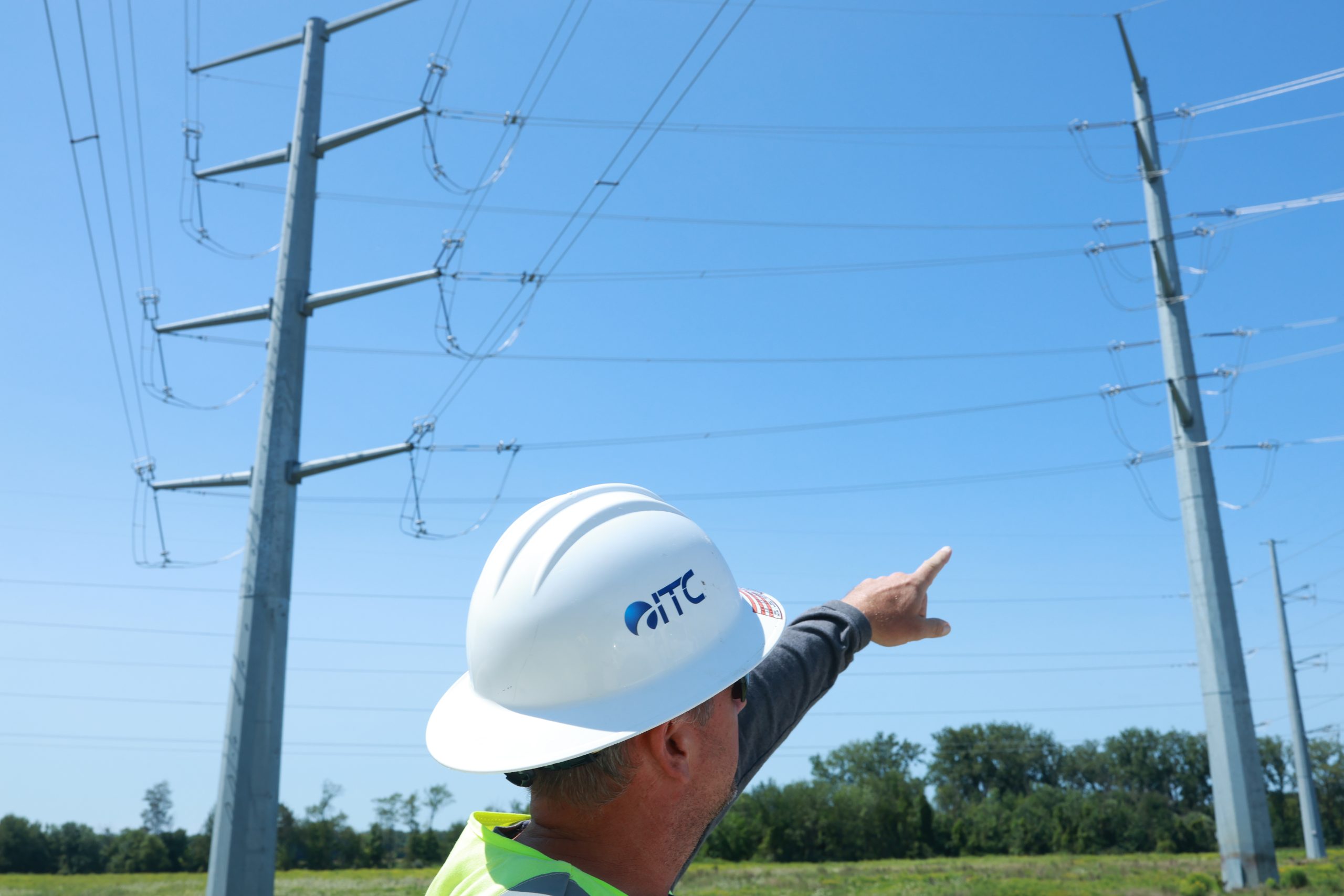 ITC field representative in hard hat pointing to transmission monopole.