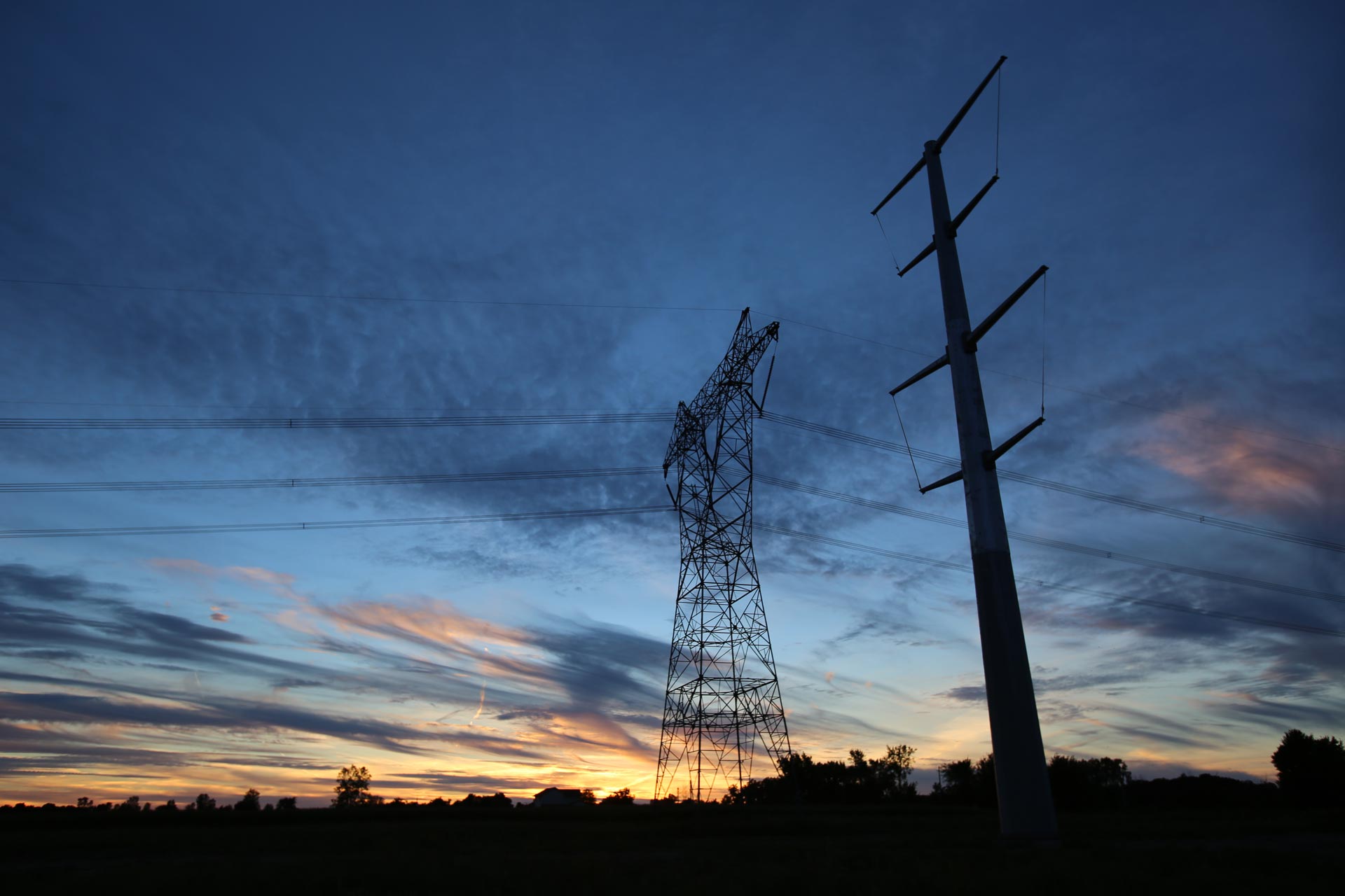 Two types of transmission lines in sky at dusk in Michigan.
