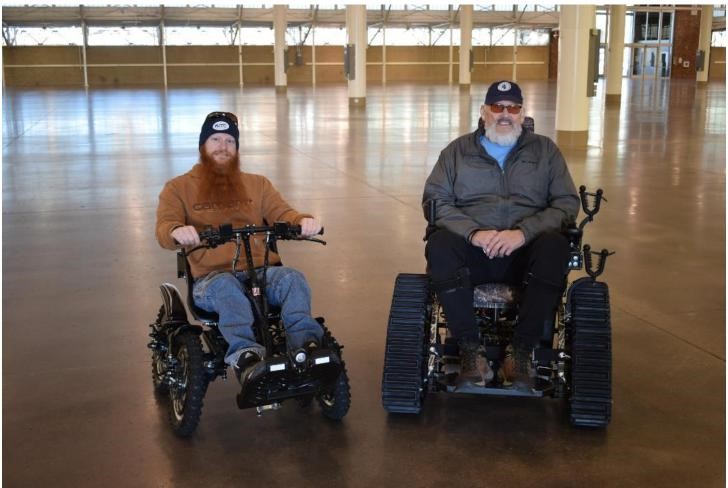 Two people in action track chairs posed for a photo inside a building.