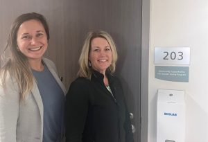 Two people posed outside of a room at medical center with a sign that says generously supported by ITC Greater Giving Program.