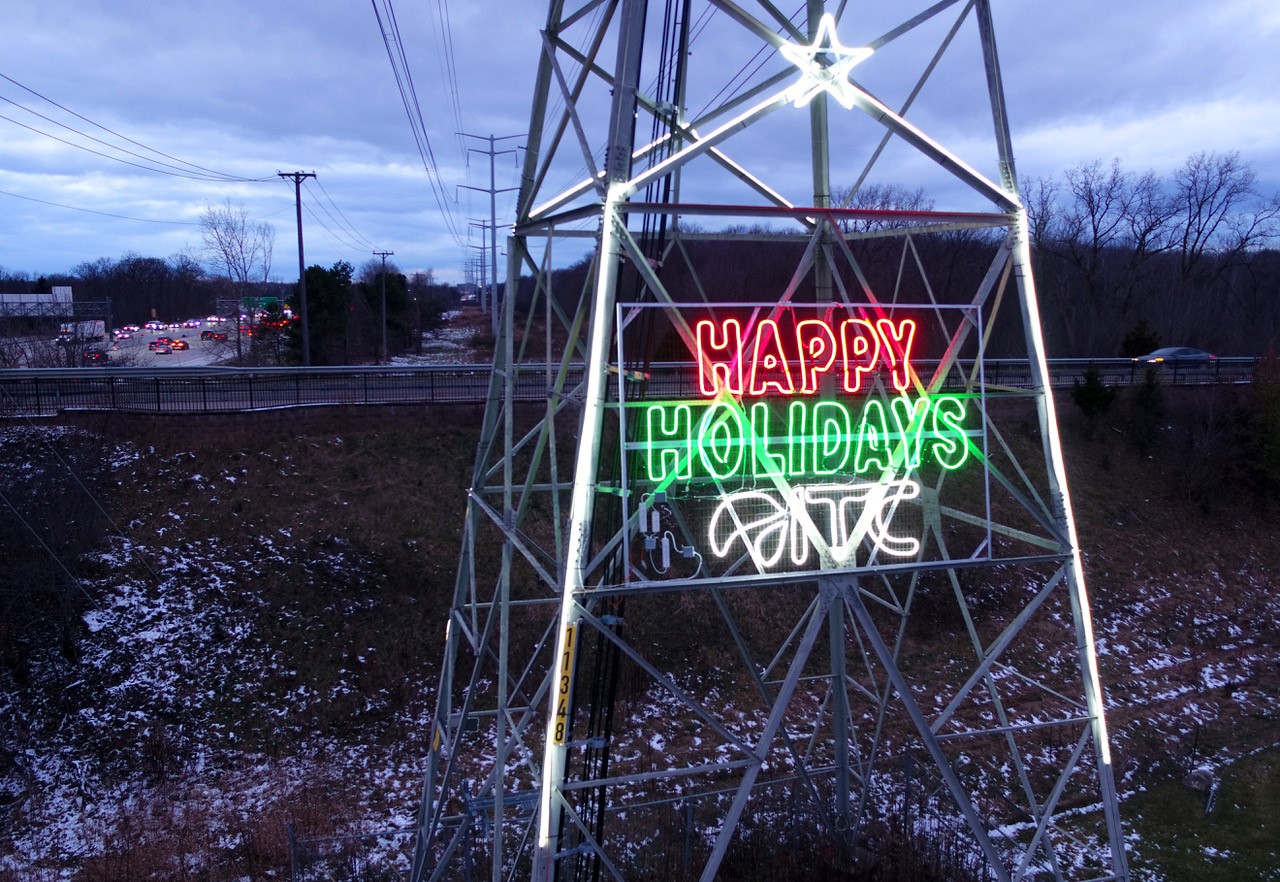 Transmission tower at dusk with holiday lights and message from ITC.